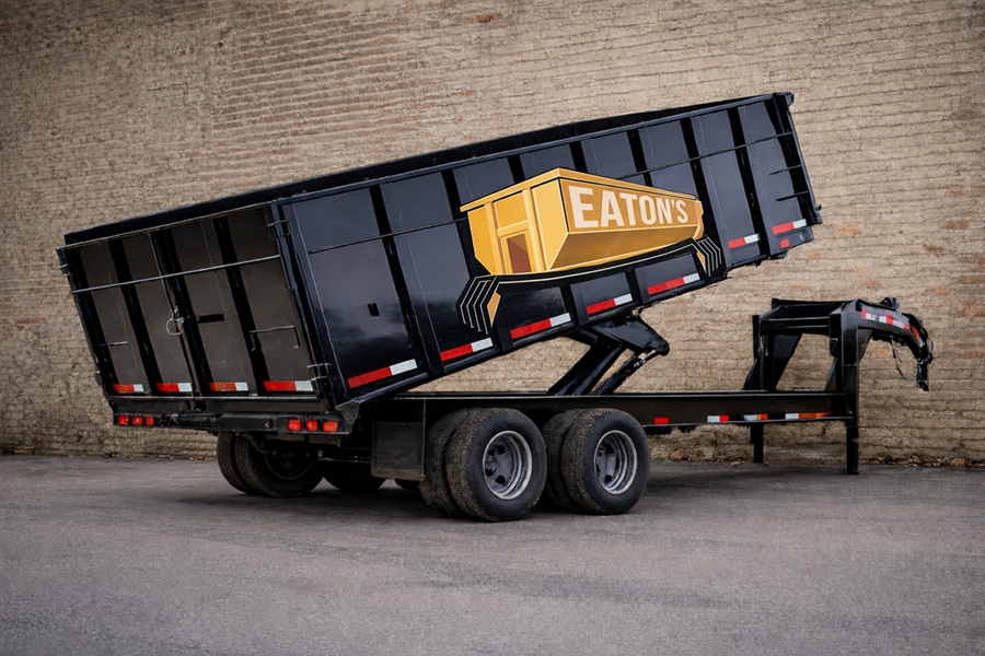 Eaton’s Construction roll-off dumpster trailer tilted for unloading against brick wall background, heavy-duty waste container for construction debris removal.