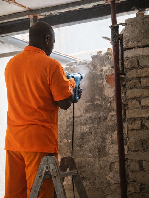 Worker using power drill to remove brick wall during interior demolition and renovation project.