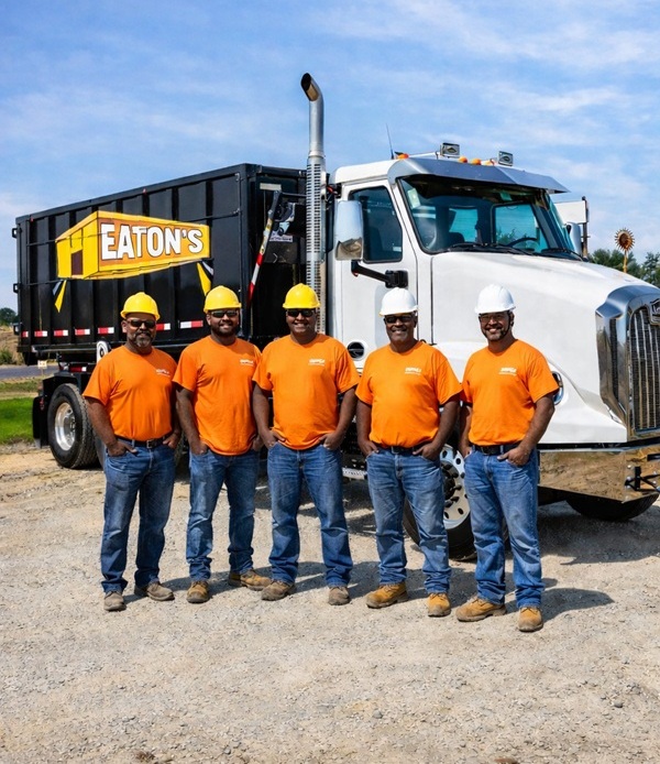 Eaton’s Construction team members in safety helmets standing in front of branded dumpster truck, professional waste removal and dumpster rental crew.